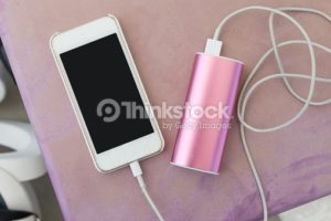 mobile phone in plastic case plugin to a power bank charger through a charging cable, on old pinkish purple outdoor plastic table
